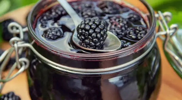 Słoik pełen dżemu z jeżyn, z jedną jeżyną na łyżeczce. Idealny sposób, by zachować smak lata i wiedzieć, co można zrobić z jeżyn.