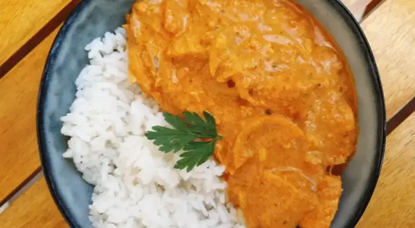 Aksamitny butter chicken w kremowym sosie, podany z ryżem i listkiem pietruszki. Pyszne danie na drewnianym stole.