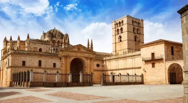 Imponente catedral románica en España, con su torre campanario y cúpula, bajo un cielo azul con nubes.