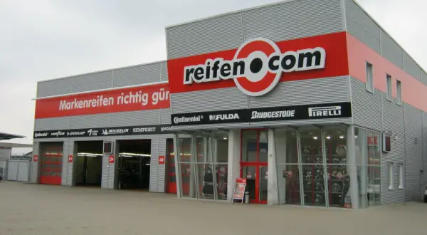 Fassade des reifen.com-Geschäfts mit roten Rolltoren und Reifenregalen im Fenster.