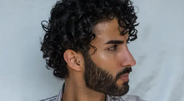 Hombre con pelo rizado oscuro y barba. Un ejemplo de como peinar pelo rizado hombre para un look natural y definido.