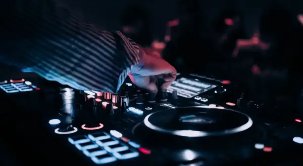 Dłoń DJ-a regulująca pokrętła na konsoli, w tle rozmyte światła.
