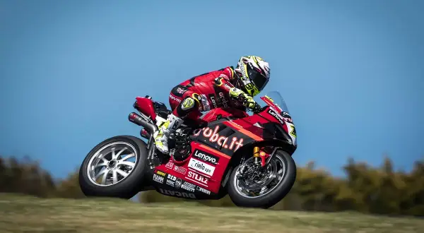 Piloto de SBK hoy en acción, con su moto Ducati roja y negra, inclinándose en una curva.