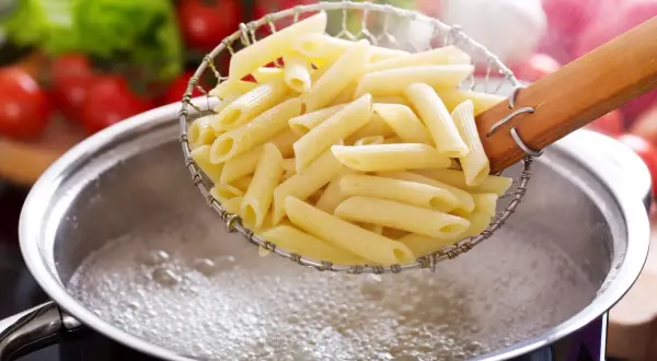 Penne w cedzaku nad garnkiem z wrzącą wodą. Czas, ile gotuje się makaron, zależy od jego rodzaju.