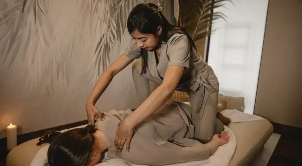Terapeuta wykonuje masaż shiatsu na osobie leżącej na macie. Relaksująca atmosfera z subtelnym oświetleniem.