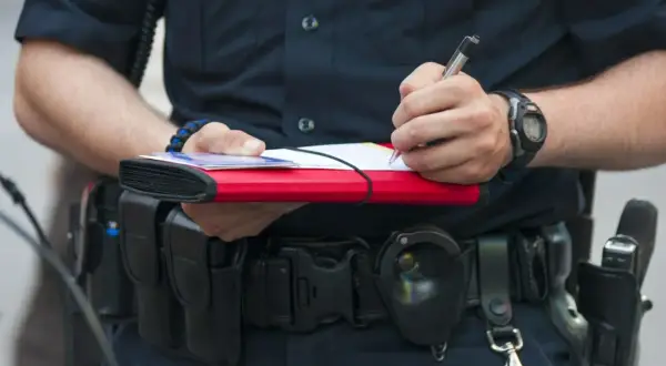 Policjant spisuje mandat. Dowiedz się, jak zapłacić mandat przelewem, by uniknąć dodatkowych kosztów.