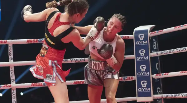 Two female boxers in a strawweight boxing match exchange punches in the ring. One boxer lands a blow to the other's face.