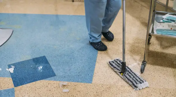 Persona con camice blu lava linoleum con alcool, usando uno straccio.