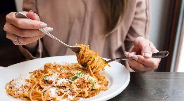 Une personne déguste une assiette de spaghetti à la sauce tomate et au parmesan. Une recette de pâtes parfaite pour un repas réconfortant.