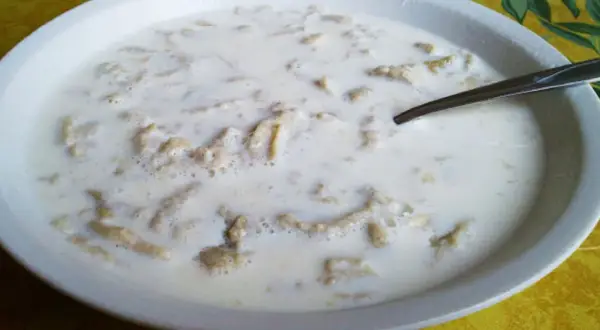 Miseczka pełna ciepłego mleka z makaronem typu zacierki, idealna na chłodny poranek.