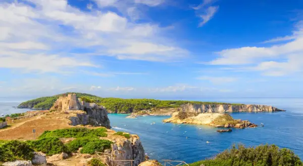 Un antico castello domina le isole della Puglia, con acque azzurre e vegetazione lussureggiante.