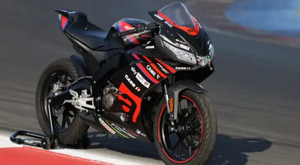 Czarny motocykl Aprilia 125 na torze wyścigowym. Zastanawiasz się, ile jedzie motor 125? Ten sportowy model jest gotowy do akcji.