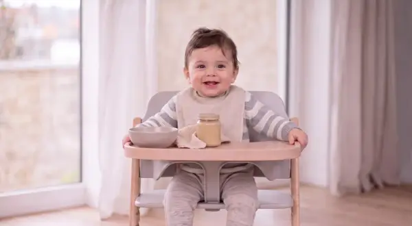 Ein lächelndes Baby sitzt im Hochstuhl, bereit für Brei. Was kann ein Baby mit 9 Monaten? Es kann schon viel, wie dieses fröhliche Kind beweist!