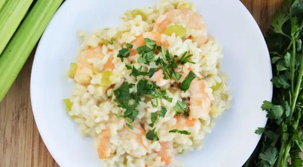 Pyszne risotto z krewetkami, ozdobione natką pietruszki, obok łodygi selera i oliwy.