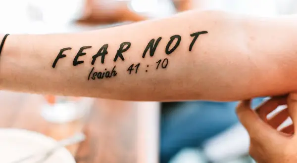 Tatuaż a religia: napis "FEAR NOT" z cytatem z Izajasza 41:10 na przedramieniu.