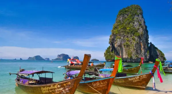 Träbåtar guppar i det turkosa vattnet vid Koh Hong. En imponerande klippa reser sig ur havet.