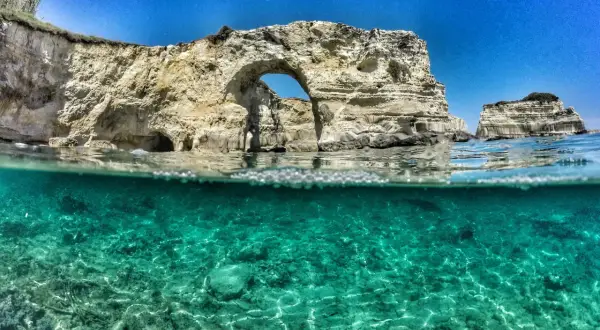 Arco naturale e faraglioni nel mare cristallino del Salento, il mare più bello. Acqua turchese e rocce bianche sotto un cielo azzurro.