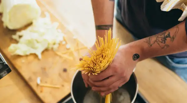 Hände mit Tattoos halten Spaghetti über einen Topf. Das bedeutet al dente: perfekt gekochte Pasta.