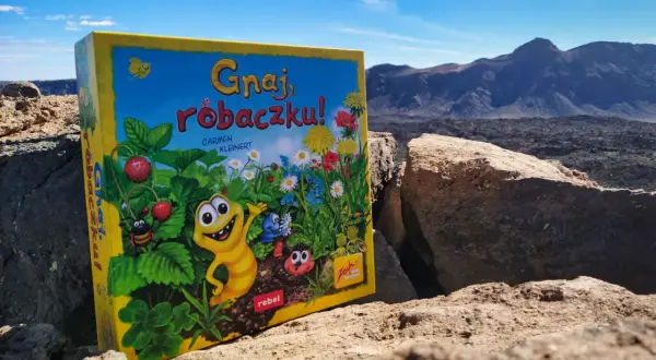 Gnaj, robaczku!" - planszówka z wesołymi robaczkami i truskawkami, na tle surowego krajobrazu.