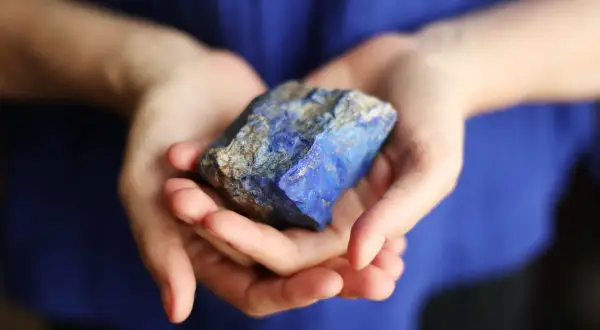 Manos sostienen un trozo de lapislázuli, su intenso azul resalta contra la tela azul.