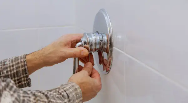 Mani che lavorano per smontare miscelatore doccia a muro.
