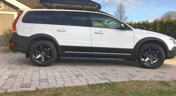 Vit Volvo XC70 2016 med takbox och svarta fälgar. Kanske ett problem med att få plats med allt bagage?