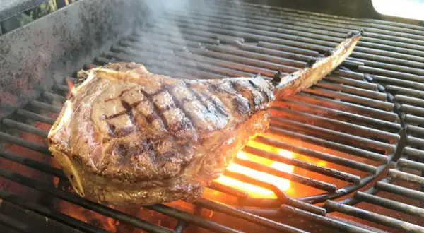 Ein saftiges Tomahawk Steak grillen, mit sichtbaren Grillstreifen und Flammen darunter.