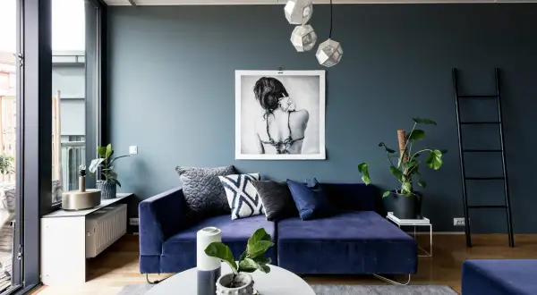 Ein tiefes, modernes Blau dominiert diesen Wohnraum. Ein Samtsofa in diesem Farbton lädt zum Entspannen ein, während ein Kunstwerk und geometrische Lampen Akzente setzen.