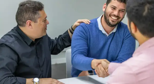 Hombres estrechando manos y sonriendo. Uno pone una mano en el hombro del otro, como si cerraran un trato importante, quizás sobre cómo es obligatorio tener seguro de hogar.