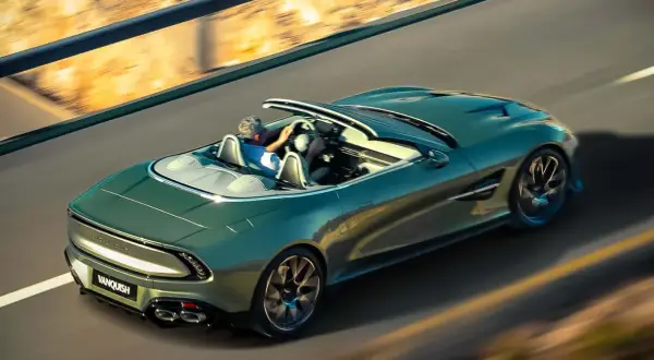 Zielony Aston Martin Vanquish bez dachu pędzi po pustej drodze, kierowca cieszy się wolnością.