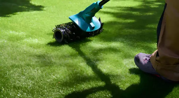 Persona realizando mantenimiento de césped artificial con un cepillo eléctrico.