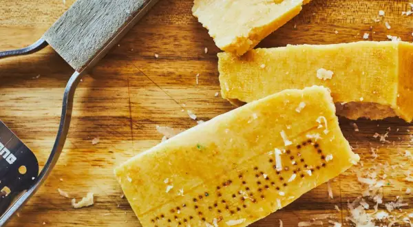 Des morceaux de **croûte parmesan comestible** sur une planche en bois, avec un râpe à fromage.