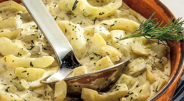 Cremige geschmorte Gurken mit Dill in einer Terrine, serviert mit einer Schöpfkelle.