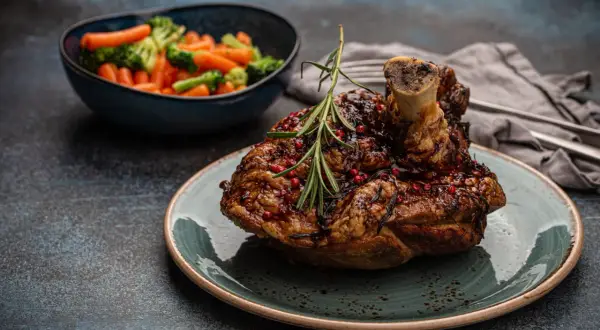 Un savoureux jaret de porc rôti, glacé et parsemé de baies roses, servi avec des légumes vapeur.