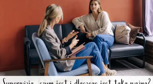 Dwie kobiety rozmawiają w przytulnym wnętrzu. Jedna z nich, siedząca w fotelu, gestykuluje, prowadząc rozmowę. Druga, na kanapie, słucha uważnie. To obraz wspierającej superwizji, kluczowej dla rozwoju zawodowego.