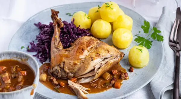 Rezept Hasenbraten im Backofen: Saftiges Kaninchen mit Klößen, Rotkohl und Sauce auf einem Teller.