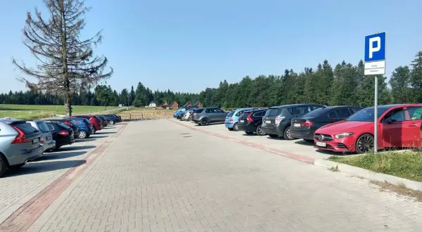 Parking przy górze Jagodnej. Samochody zaparkowane na utwardzonym placu, w tle las i domki.