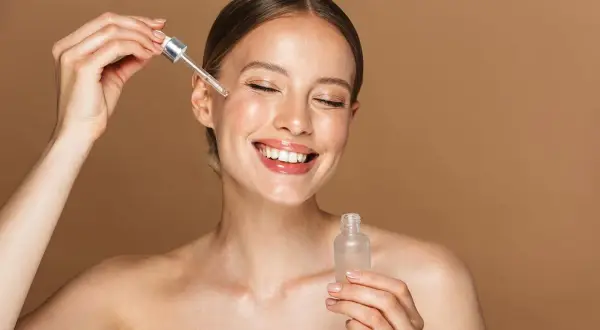 Uśmiechnięta kobieta aplikuje serum z niacynamidem. Dowiedz się, jak stosować niacynamid dla promiennej cery.