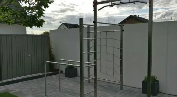 Eine Klimmzugstange für draußen mit Kletternetz und Barren im Garten. Perfekt für ein Outdoor-Workout.
