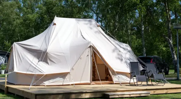 Stor glampingtält i Mölle med träaltan och solstolar. En bil syns i bakgrunden.