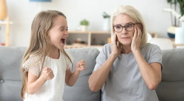 Rozkrzyczane dziecko nie może usiedzieć w miejscu, a babcia zakrywa uszy, próbując zapanować nad chaosem.