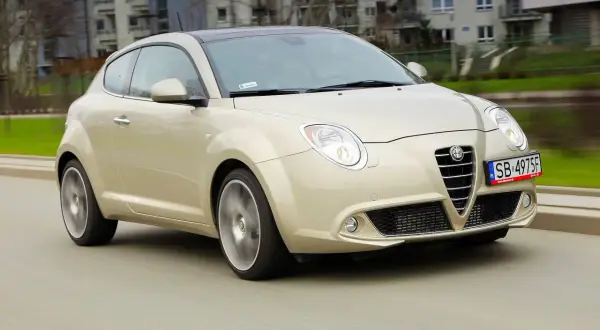 Złoty Alfa Romeo MiTo w ruchu miejskim. Wiele osób chwali ten model za wygląd, co potwierdzają alfa romeo mito opinie.