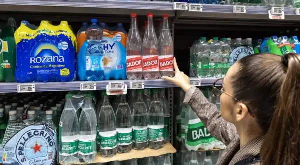 Une femme choisit une bouteille d'eau minérale Badoit. Les étiquettes indiquent la composition et le prix.