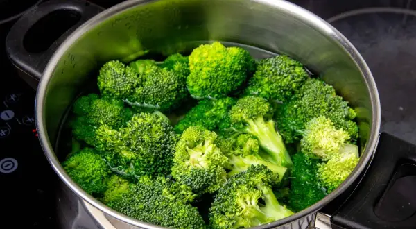 Brotes de brócoli frescos y verdes sumergidos en agua hirviendo en una olla de metal. Preparando para cocer brócoli.