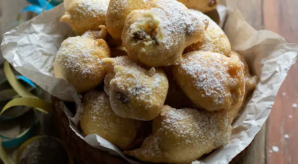 Frittelle di una volta, dolci e soffici, cosparse di zucchero a velo, in un cesto con coriandoli.