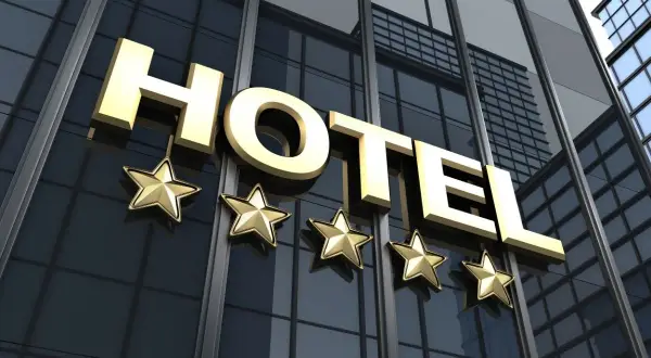 Złoty napis HOTEL z pięcioma gwiazdkami na tle nowoczesnego budynku hotelowego.