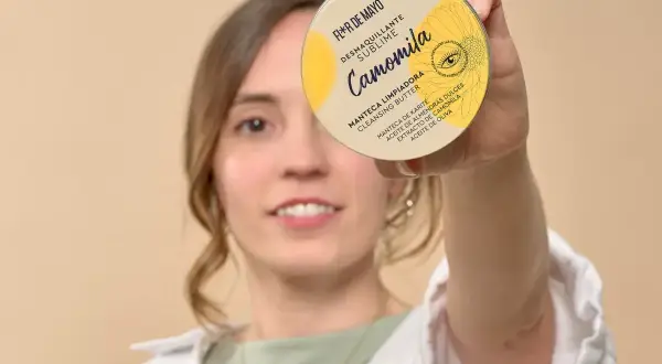 Mujer sonriente sostiene un desmaquillante en crema, "Camomila", que es un sebo limpiador con manteca de karité.