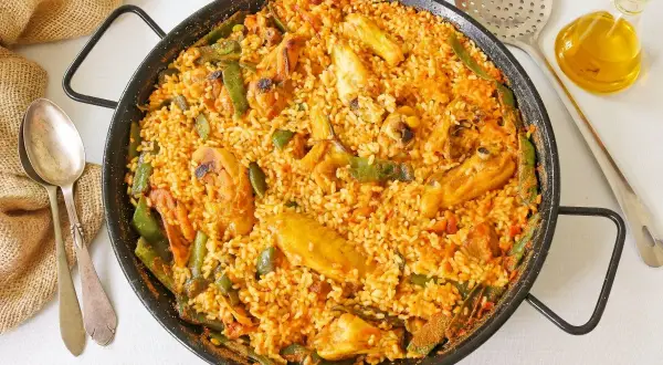 Paella de pollo recién hecha, con trozos de pollo dorado, judías verdes y arroz sabroso en una paellera.