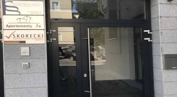 Wejście do budynku z tabliczkami: Kancelaria Radców Prawnych, Apartamenty 7a, Kancelaria Doradcy Finansowego SKORECKI.
