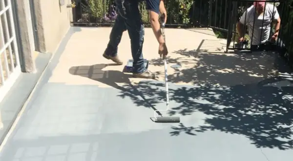 Peinture carrelage extérieur avant après : un homme peint une terrasse grise avec un rouleau, transformant l'espace.